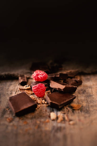 cassé la barre de chocolat avec des framboises mûres rouges sur fond marron foncé près vers le haut, macro - brown chocolate candy bar close up photos et images de collection