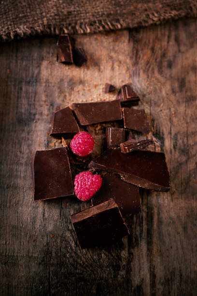 cassé la barre de chocolat avec des framboises mûres rouges sur fond marron foncé près vers le haut, macro - brown chocolate candy bar close up photos et images de collection