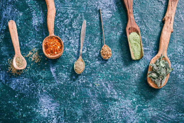 Dried herbs for cooking Dried chili peppers, coriander, tarragon, thyme, oregano and lemon balm in various spoons over dark blue spotty background. Top view tarragon cutting board vegetable herb stock pictures, royalty-free photos & images