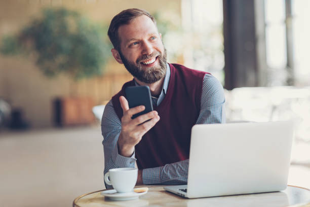 istock Bearded man with smart phone and laptop in cafe 693423546