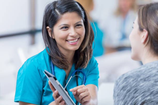 Healthcare professional uses a digital tablet Cheerful mid adult Asian healthcare professional points to something on a digital tablet while talking with female patient. triage stock pictures, royalty-free photos & images