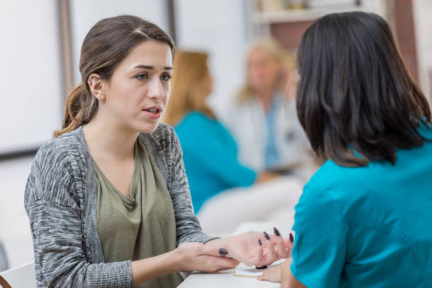Concerned woman talks with triage nurse about injury Worried young Caucasian woman talks with triage nurse about her injured hand. The patient has a concerned expression on her face. triage stock pictures, royalty-free photos & images