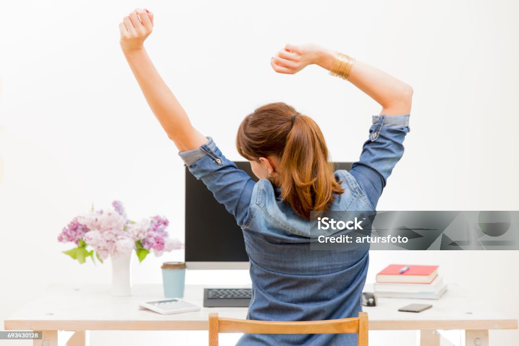 Woman stretching her arms sitting by the table at work next to computer Ergonomics Stock Photo