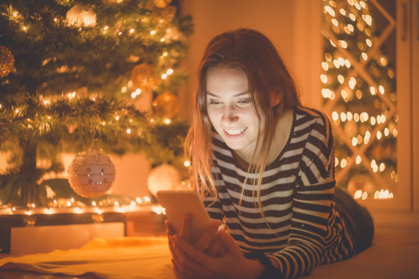 istock Young female using smartphone next to the Christmas tree at home 693436136