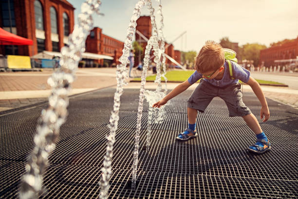 Little boy playing with fountain on a hot summer day. Hot summer day in the city. Little boy is having fun playing in the city fountain after school. He is reaching and touching the water.
 backpack sprayer stock pictures, royalty-free photos & images