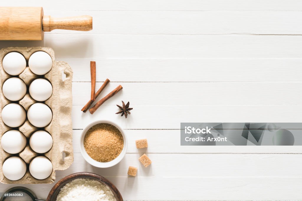 Baking ingredients / cooking food bread pastry or cake Baking ingredients on white wood with copy space. Eggs, brown sugar, white flour, spices and rolling pin on white wooden background. Top table top view. Cooking, baking background, recipe mock up Flour Stock Photo