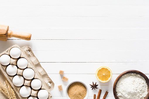 Baking ingredients on white wood with copy space. Eggs, brown sugar, white flour, spices and rolling pin on white wooden background. Top table top view. Cooking, baking background, recipe mock up