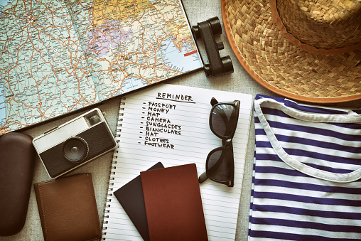 Top view of traveler's accessories and travel checklist. Vintage style photo filter with grain and vignette added.
