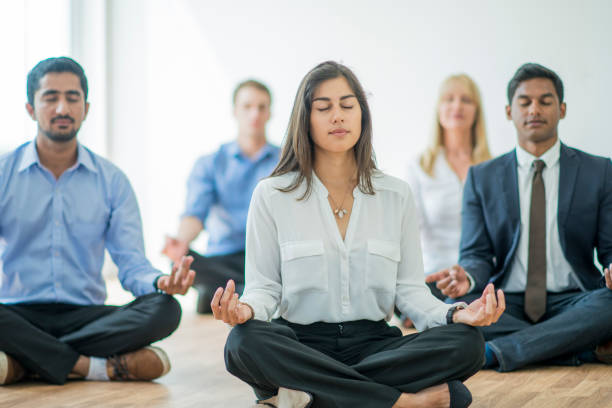 Meditating at the Office A multi-ethnic group of young business men and women in semi-casual office clothes are sitting on the floor and meditating to relax in an indoor, sunlit office. meditating photos stock pictures, royalty-free photos & images