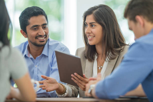 Digital Technology in a Business Meeting A multi-ethnic group of young business men and women in semi-casual office clothes are sharing ideas and holding a digital tablet in an indoor, sunlit office. indian ethnicity stock pictures, royalty-free photos & images