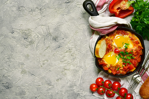 Shakshuka-traditional israeli tomato stew with eggs in a cast iron pan on a grey slate,stone or concrete background.Top view with copy space.