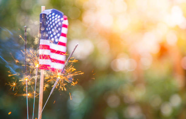 A stock photo of a USA stars and stripes flag with sparklers in the foreground. Perfect for designs and articles about the 4th of July and the USA.
