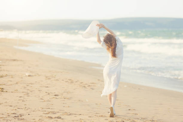 Beautiful young woman with white dress walking on the beach. Concept of the female solo traveler.