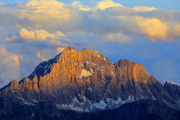 Snow-dusted fields stretch towards rugged mountain peaks under a cloudy sky. Moody landscape showcasing twilight in the alpine region.