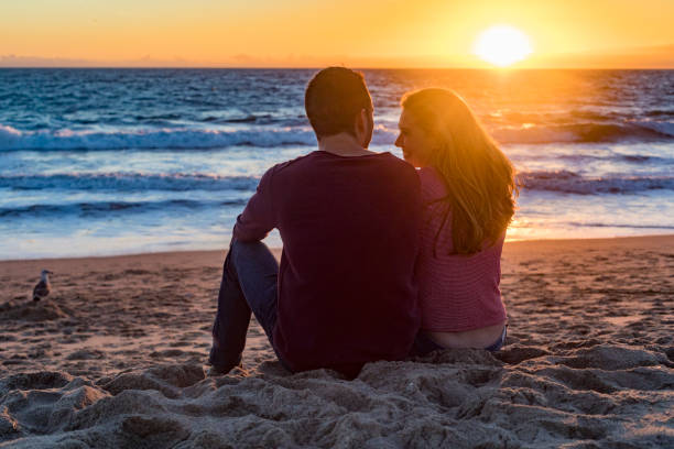 istock Happy Young Couple Sitting on the Beach at Sunset 693547280