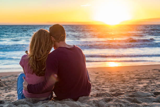 Happy young couple sitting on the beach at sunset on Venice Beach in Los Angeles, California, USA