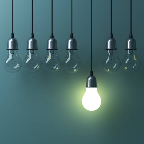 istock One hanging light bulb glowing different and standing out from unlit incandescent bulbs with reflection on green background , leadership and different business creative idea concept. 3D render 693551126