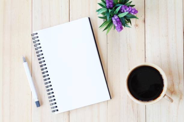 istock Top view image of open notebook with blank pages and coffee cup on wooden background, ready for adding or mock up 693567120