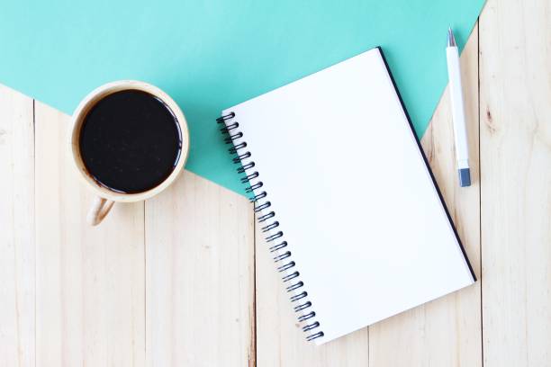 istock Top view image of open notebook with blank pages and coffee cup on wooden background, ready for adding or mock up 693567122