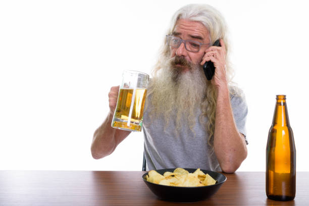 foto de estúdio de sênior homem barbudo falando no celular com copo de cerveja com o prato de batatas fritas na mesa de madeira - beer glass mustache beer color image - fotografias e filmes do acervo