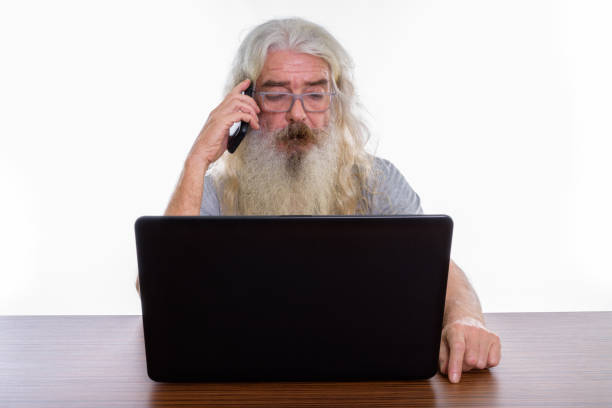 istock Studio shot of senior bearded man talking on mobile phone while using laptop on wooden table 693579838
