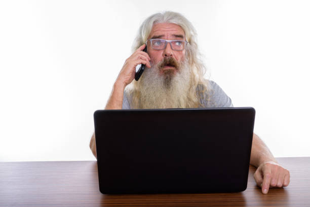 istock Studio shot of senior bearded man thinking while talking on mobile phone and using laptop on wooden table 693579856