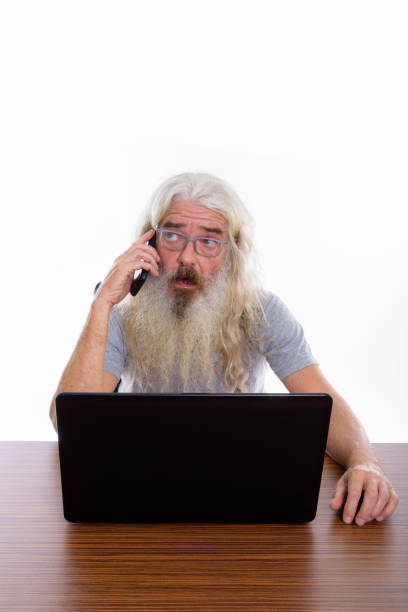 istock Studio shot of senior bearded man thinking and talking on mobile phone while using laptop on wooden table 693579862