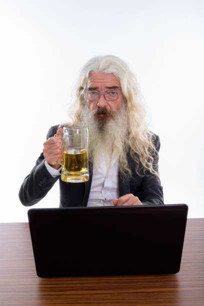 studio um shot de sênior empresário barbudo segurando o copo de cerveja com o laptop na mesa de madeira - beer glass mustache beer color image - fotografias e filmes do acervo