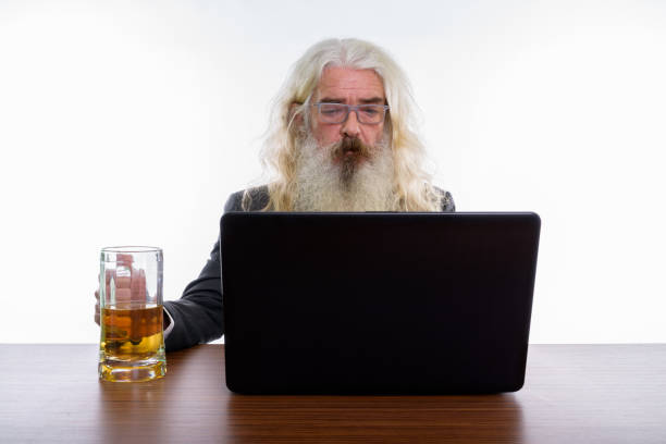 studio um shot de sênior empresário barbudo usando laptop com copo de cerveja na mesa de madeira - beer glass mustache beer color image - fotografias e filmes do acervo