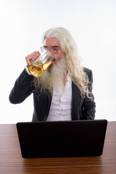 foto de estúdio do copo de bebida de homem de negócios sênior barbudo de cerveja com o laptop na mesa de madeira - beer glass mustache beer color image - fotografias e filmes do acervo