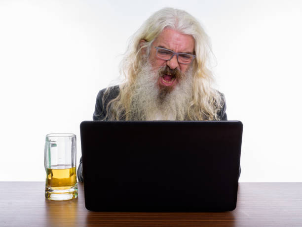 studio uma dose de raiva empresário barbudo sênior gritando enquanto usando laptop com copo de cerveja na mesa de madeira - beer glass mustache beer color image - fotografias e filmes do acervo