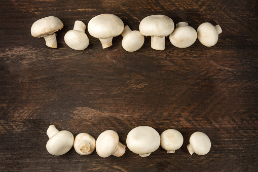 An overhead photo of fresh white mushrooms on a dark rustic texture with a place for text
