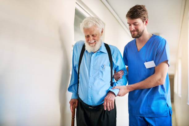 Taking small steps toward recovery Shot of a young doctor helping his senior patient walk down a hallway in hospital walking aide stock pictures, royalty-free photos & images