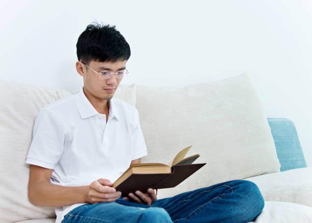 istock Young asian man reading a book at home 693608108