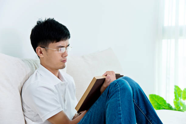 istock Young asian man reading a book at home 693610188