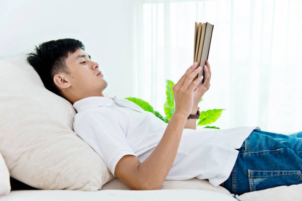 istock Young asian man reading a book at home 693610348