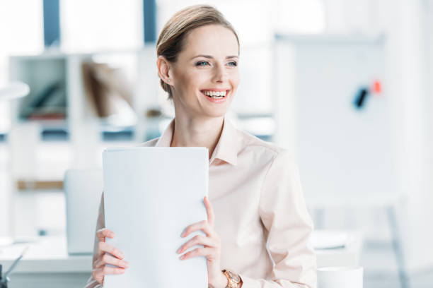 istock young smiling businesswoman holding documents while sitting at office 693610504
