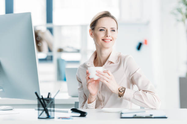 istock young smiling businesswoman drinking coffee while sitting at office 693610870
