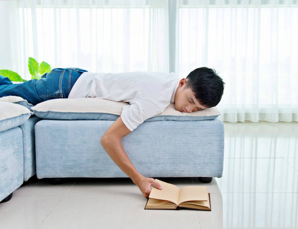 istock Young asian man with book asleep on sofa 693611012