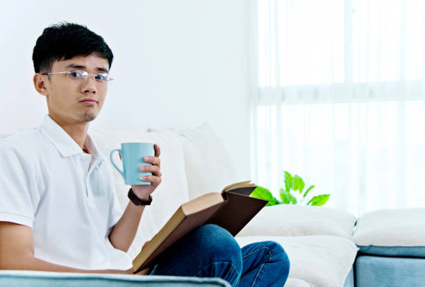 istock Young asian man drinking coffee and reading book 693611354