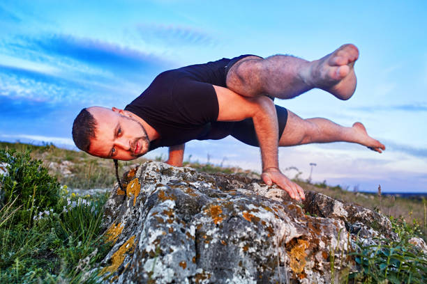 istock Attractive man doing yoga on the stone against bright blue sky with clouds. 693613742