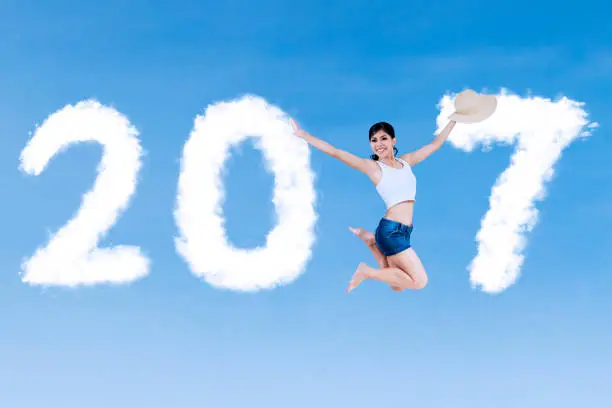 Concept of New Year 2017. Pretty woman jumping on the blue sky with clouds shaped number 2017