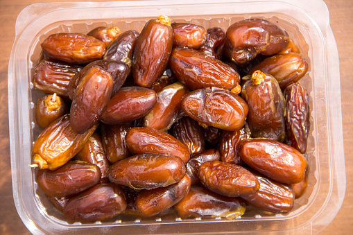 Dried date fruits in plastic container on wooden table. Top view