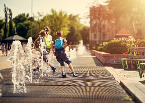 Kids running between fountains on a hot summer day. Hot summer day in the city. School children are having fun playing in the city fountains after school.
 backpack sprayer stock pictures, royalty-free photos & images