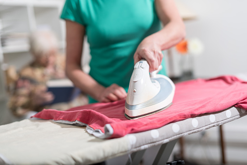 Home helper ironing clothes for elderly woman