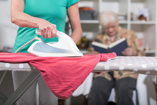 Home helper ironing clothes for elderly woman