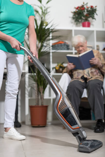 Home helper vacuuming for an old woman stock photo