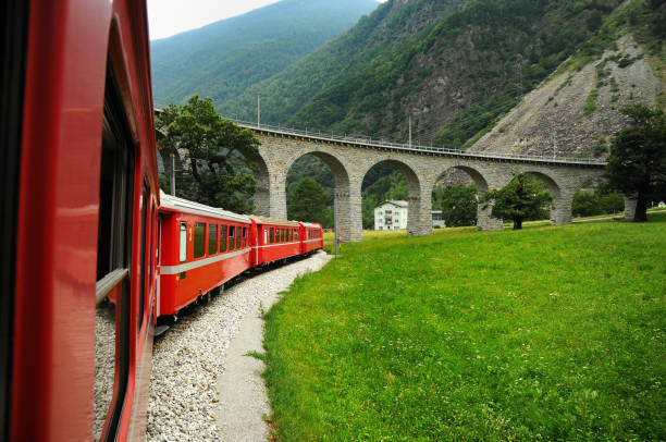 swiss red train bernina express pass on brusio viaduct. it is a spectacular helicoidal stone bridge that fits the surrounding landscape and is located on the bernina railway not far from brusio railway station in canton grisons, italy. - bernina express imagens e fotografias de stock