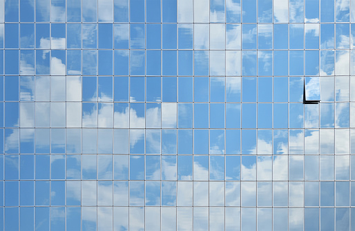 Cloudy blue sky reflection in glass windows of office business building, side view
