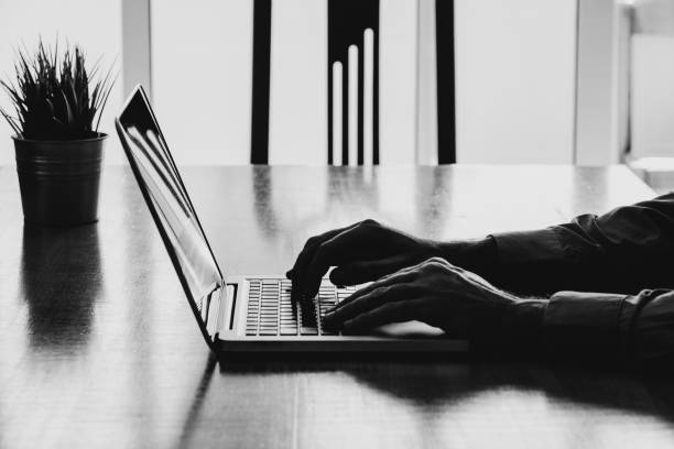 istock Man hands typing on a laptop in a workplace. Business black and white. 693655874